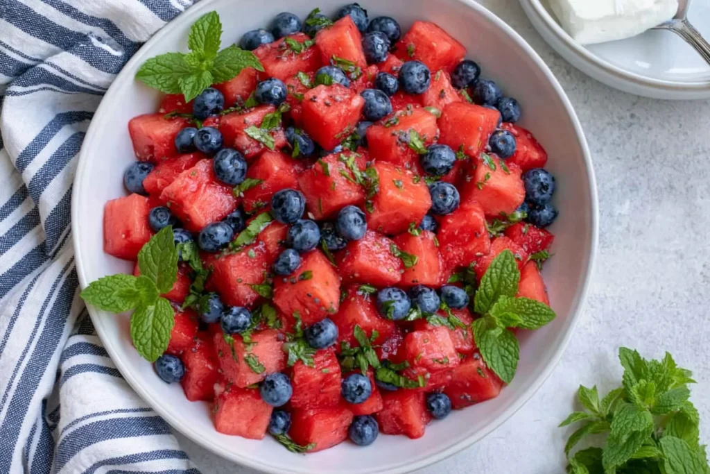 Watermelon Blueberry Salad in a white bowl with fresh mint, honey lime dressing, and juicy summer fruit