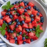Watermelon Blueberry Salad in a white bowl with fresh mint, honey lime dressing, and juicy summer fruit