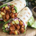 Hawaiian BBQ Chicken Wraps filled with glazed chicken, pineapple chunks, crisp lettuce, and red onion, served with lime wedges.
