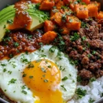 Hot Honey Ground Beef Bowls with rice, roasted sweet potatoes, avocado, a fried egg, fresh herbs, and spicy honey sauce.