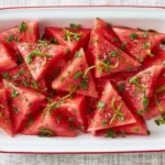 Mojito Watermelon slices with fresh mint, lime zest, black pepper, and sea salt served in a white dish