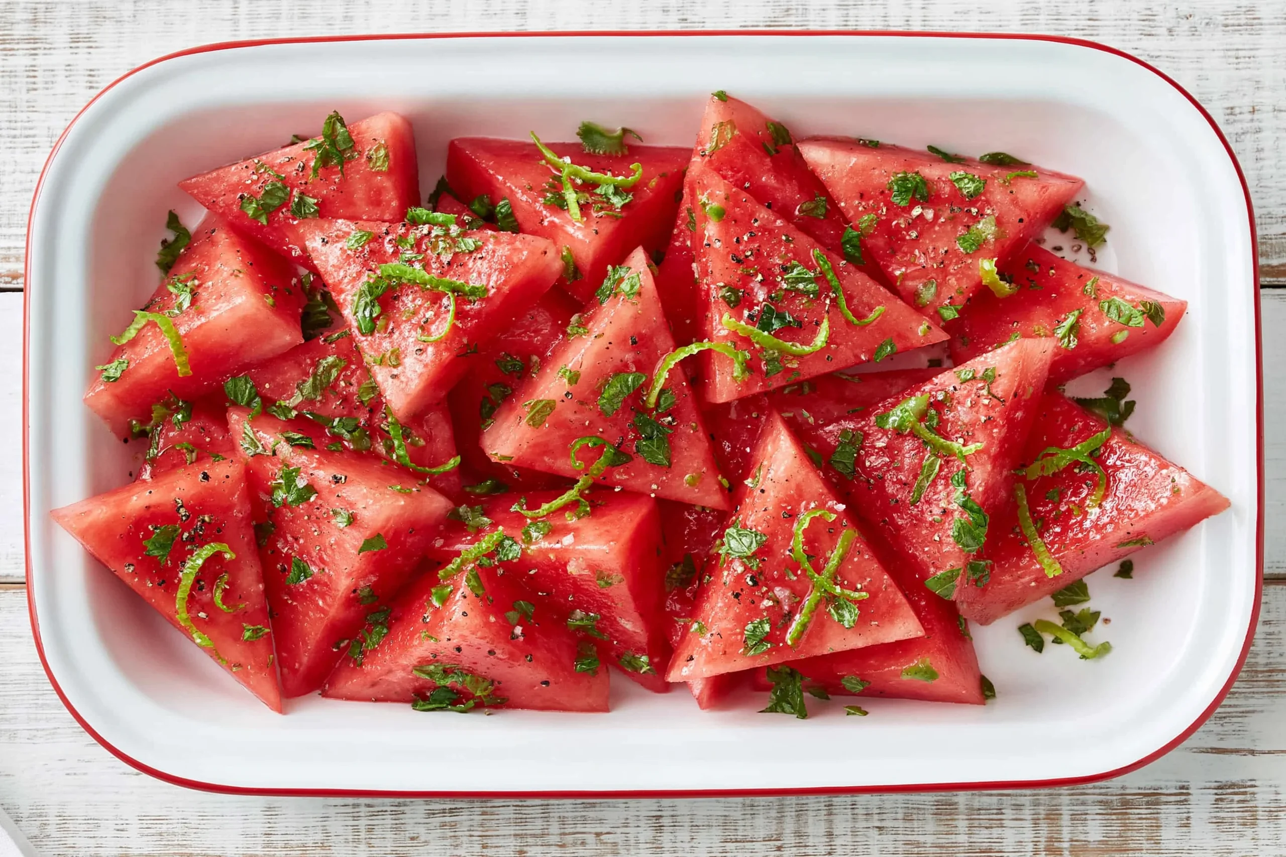 Mojito Watermelon slices with fresh mint, lime zest, black pepper, and sea salt served in a white dish