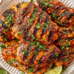 Chili Lime Grilled Chicken thighs with smoky grill marks, fresh cilantro, and lime wedges arranged on a serving platter.